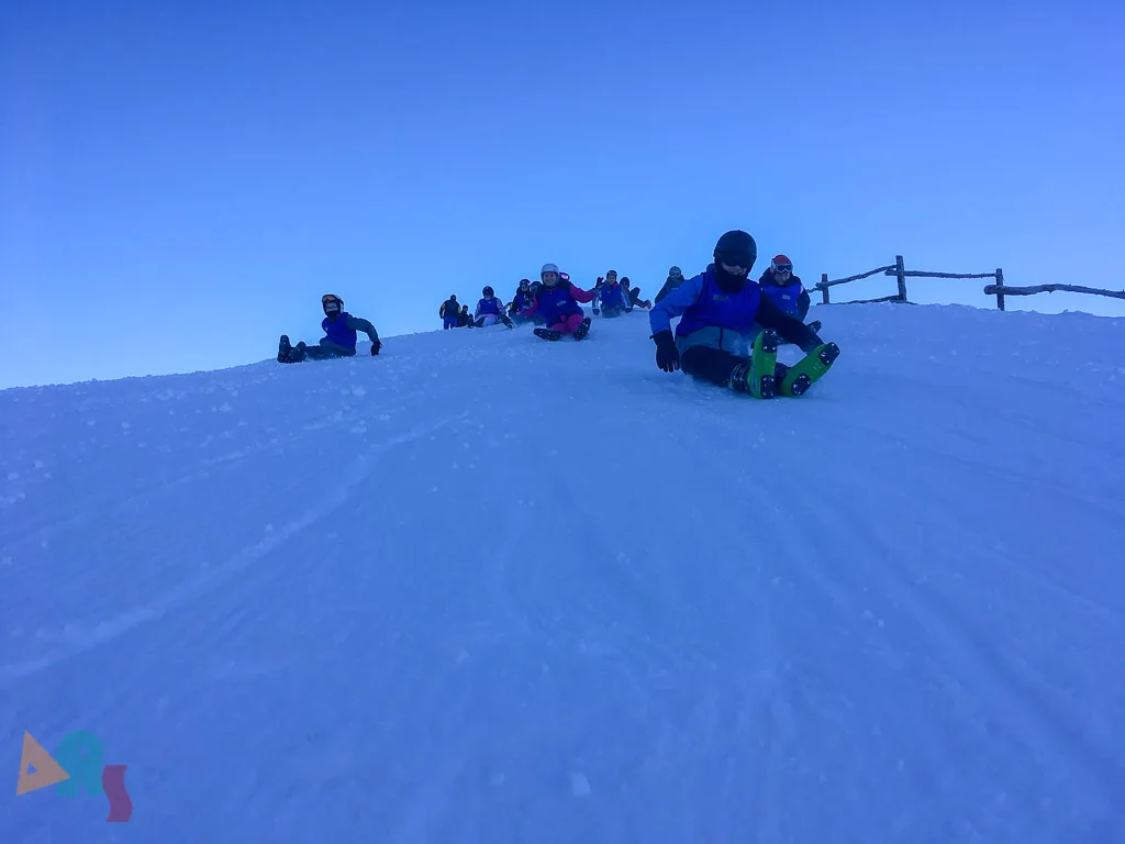 Jugendliche sitzen auf einer Schneekuppe unter blauem Himmel.